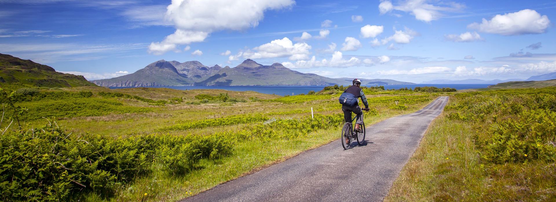 A cyclist going down a single track road with views to other islands in the distance