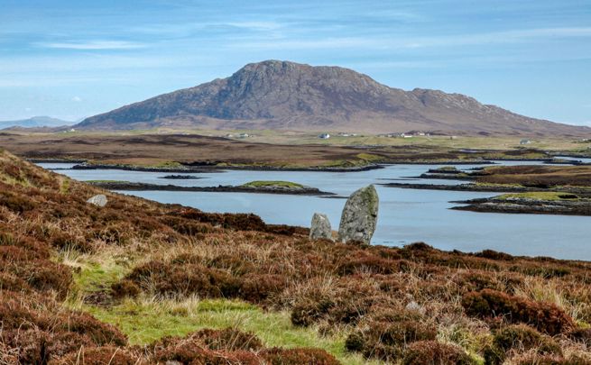 A view of an inland loch in the backgrounf with Ben Langass Stone Circle rising from the undergrowth on North Uist
