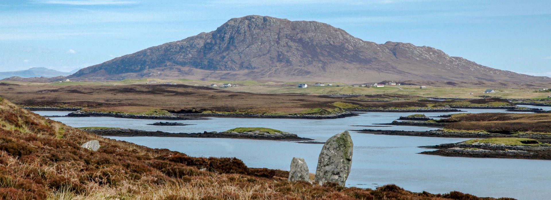 A view of an inland loch in the backgrounf with Ben Langass Stone Circle rising from the undergrowth on North Uist