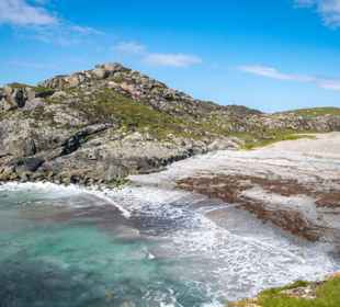 Iona coastline and bay with waves lapping the small beach, and a rocky landscape in the background.