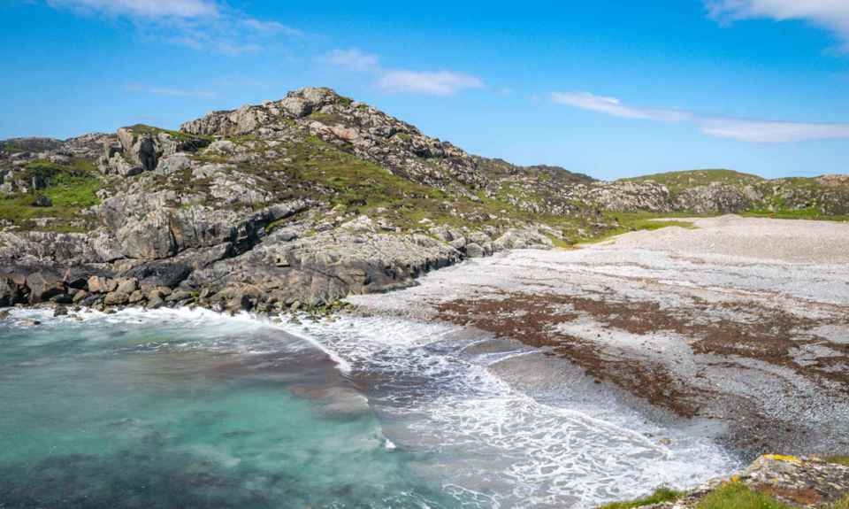 Iona coastline and bay with waves lapping the small beach, and a rocky landscape in the background.