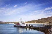 The ferry to and from Eriskay berthed on a slipway with vehicles about to drive off the lowered ramp on a beautiful sunny day.