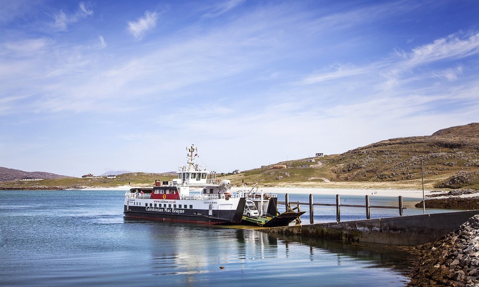 The ferry to and from Eriskay berthed on a slipway with vehicles about to drive off the lowered ramp on a beautiful sunny day.
