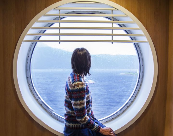 A passenger on the ferry sitting and looking out a round window