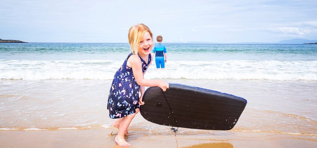 A child with a small surf board on the beach playing