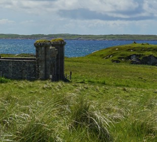 Historic stone ruin standing in grassy coastal landscape with sea views and rolling green hills in the background.