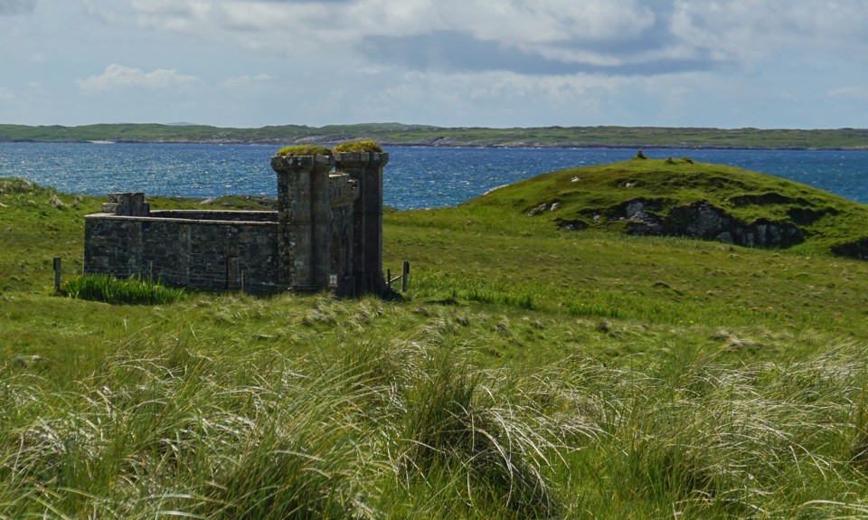Historic stone ruin standing in grassy coastal landscape with sea views and rolling green hills in the background.