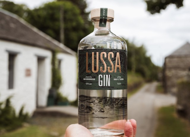 Someone holding a bottle of gin with the stables in the background