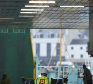 Crew member directing vehicle loading operations on board a CalMac ferry car deck.