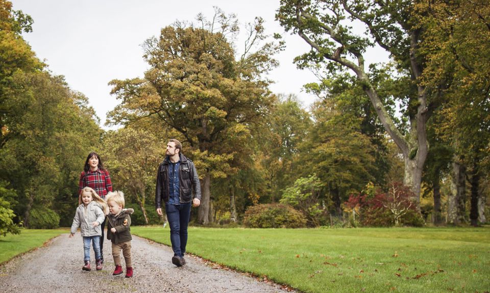 A young family of 4 enjoying a walk in a tree lined park