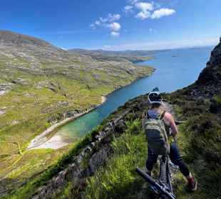 Cyclist on a high trail looking down at the green and rocky coastline.