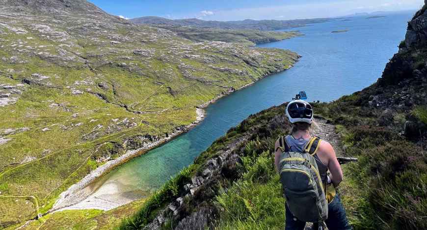 Cyclist on a high trail looking down at the green and rocky coastline.