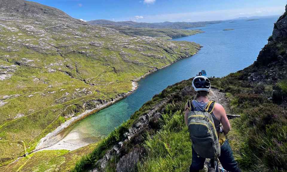 Cyclist on a high trail looking down at the green and rocky coastline.