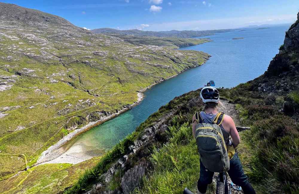 Cyclist on a high trail looking down at the green and rocky coastline.