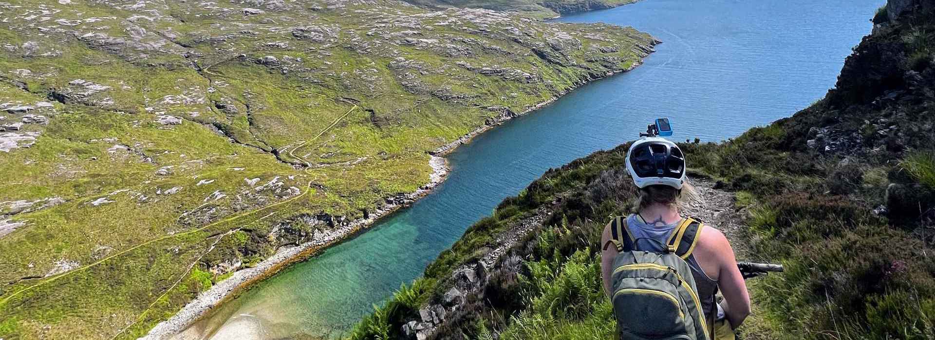 Cyclist on a high trail looking down at the green and rocky coastline.