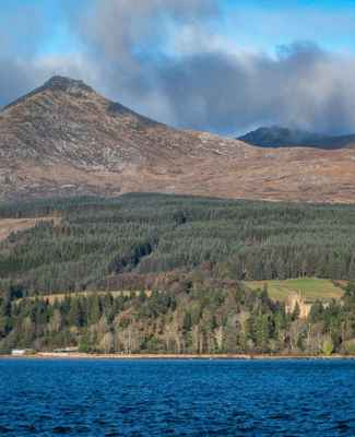 Goatfell, the highest peak on Arran, with woodland and water in the foreground.