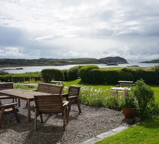Outdoor seating area overlooking a sheltered bay, with landscaped gardens, islands and dramatic clouds over the sea.