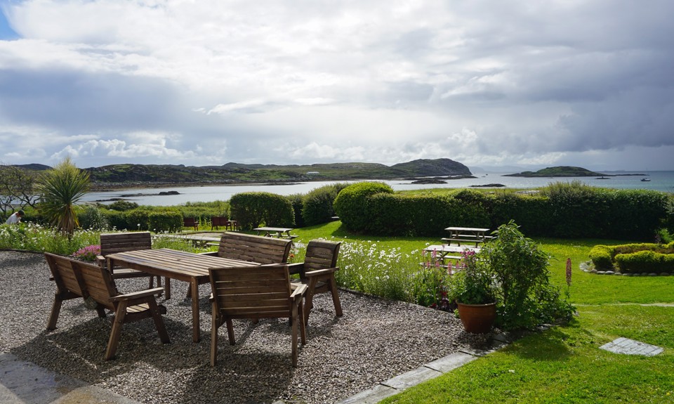 Outdoor seating area overlooking a sheltered bay, with landscaped gardens, islands and dramatic clouds over the sea.