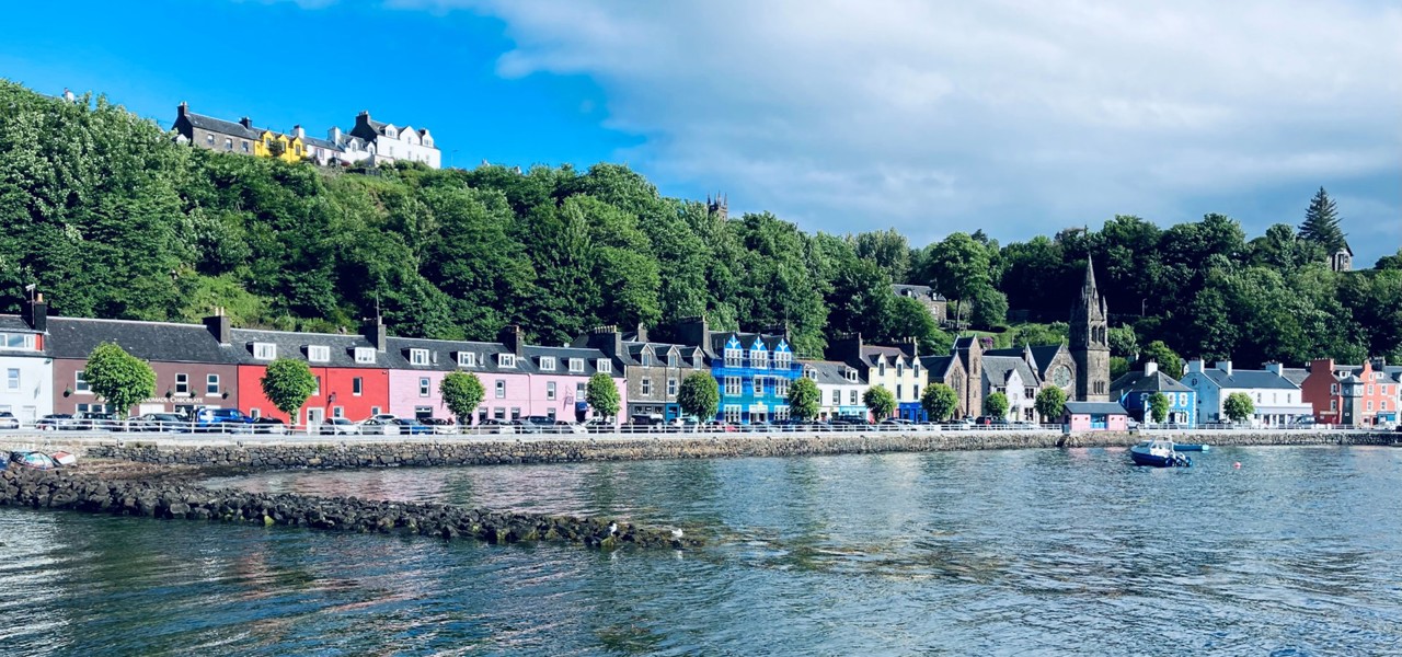 Colorful waterfront houses in Tobermory, with green hills and trees in the background.