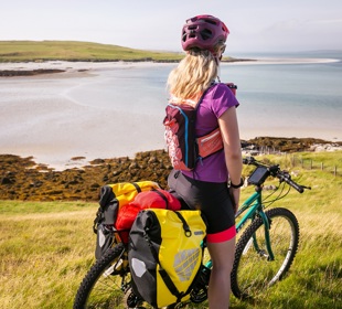 A cyclist, stopped while on her bike, admiring the views of the beach and out across the water. Lewis.