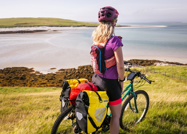 A cyclist, stopped while on her bike, admiring the views of the beach and out across the water. Lewis.