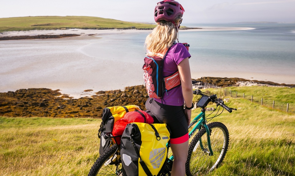 A cyclist, stopped while on her bike, admiring the views of the beach and out across the water. Lewis.