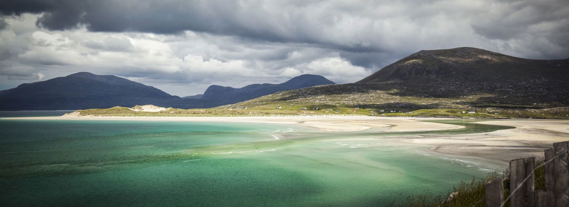 A colourful sea and sandy beach on Harris, with hills and greying clouds