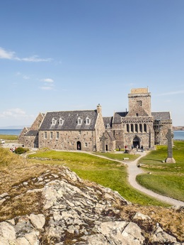 The ancient stone building of Iona Abbey taking from a rocky hilltop with the costline and water in the background.