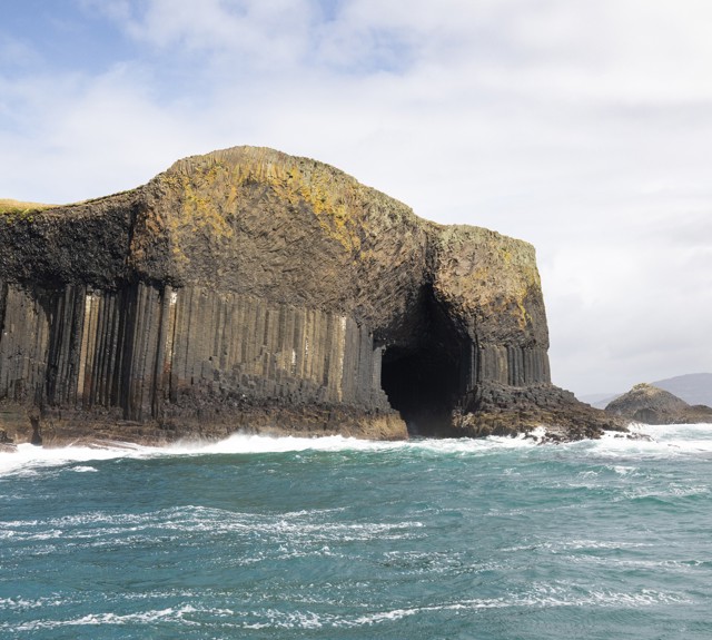 Basalt sea cliffs and cave entrance at Fingal’s Cave, with waves breaking against the rocky shoreline.