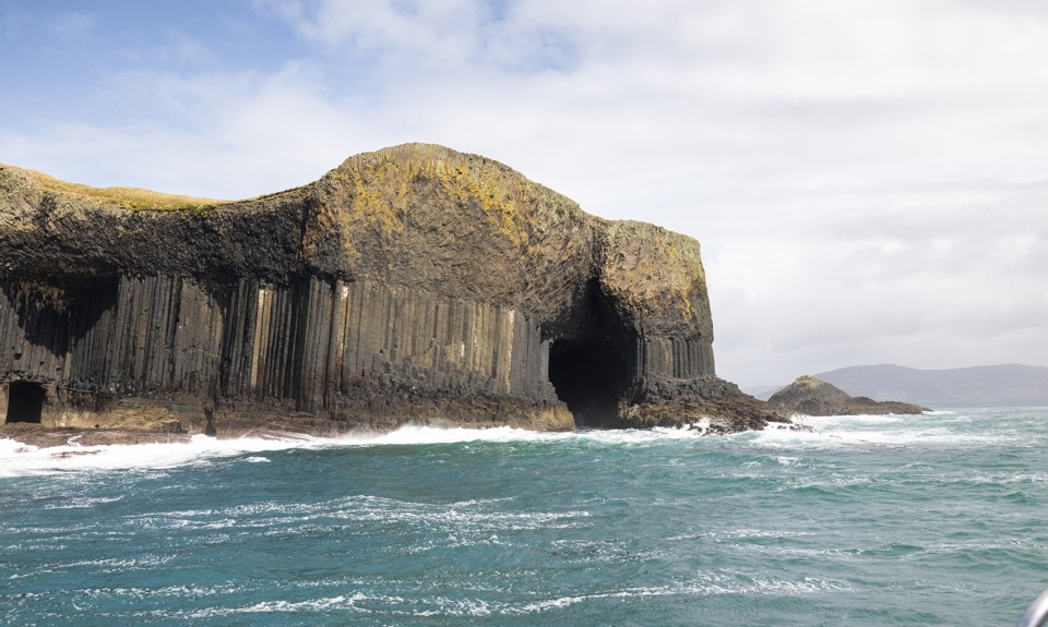 Basalt sea cliffs and cave entrance at Fingal’s Cave, with waves breaking against the rocky shoreline.
