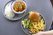 to the left a plate of katsu curry in a white and blue bowl with rice to the side of the plate. To the right a plate of burger, fries and salad