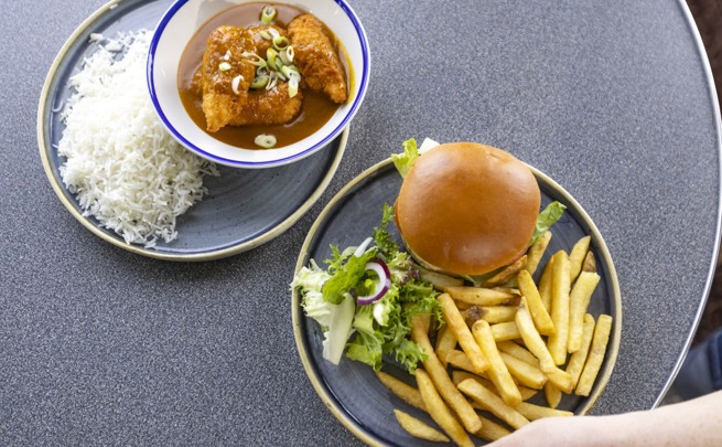 to the left a plate of katsu curry in a white and blue bowl with rice to the side of the plate. To the right a plate of burger, fries and salad