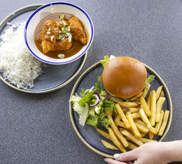 to the left a plate of katsu curry in a white and blue bowl with rice to the side of the plate. To the right a plate of burger, fries and salad