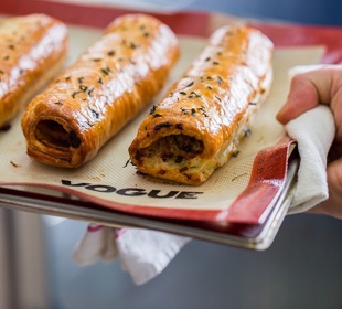 Hand holding a baking tray of sausage rolls