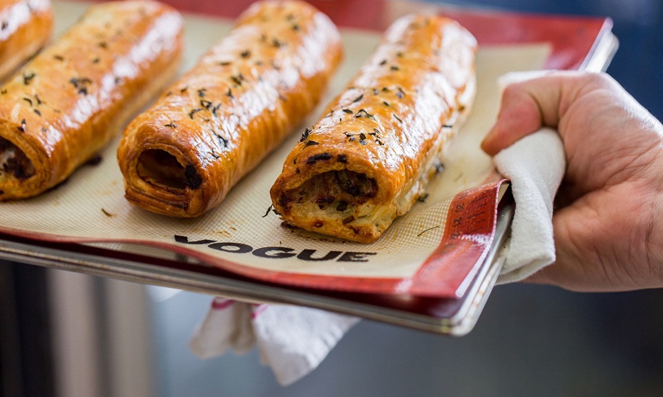 Hand holding a baking tray of sausage rolls