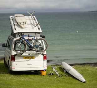 A motorhome parked by the beach and waterside, with bike, canoe and surfboard. Barra.