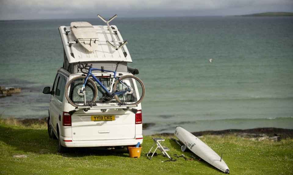 A motorhome parked by the beach and waterside, with bike, canoe and surfboard. Barra.