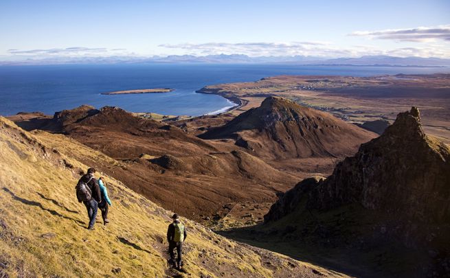 Hillwalkers descending a path. A stunning view of hill tops, coastline and across the water to the mainland.