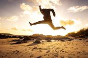 Sunset with a man jumping in a star shap on a deserted sandy beach.