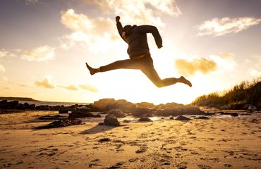 Sunset with a man jumping in a star shap on a deserted sandy beach.