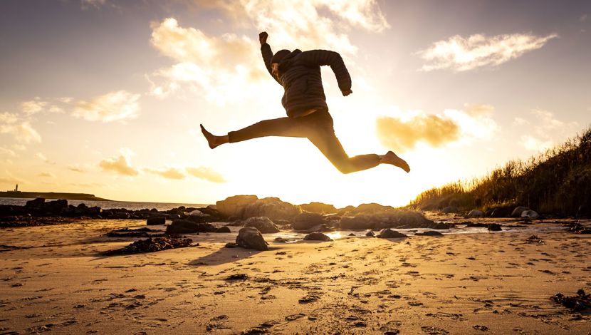 Sunset with a man jumping in a star shap on a deserted sandy beach.