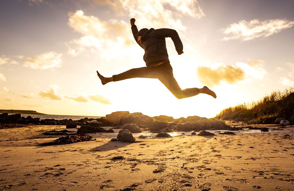 Sunset with a man jumping in a star shap on a deserted sandy beach.