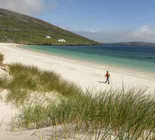 A hiker strolling along a deserted golden sandy beach on Barra.