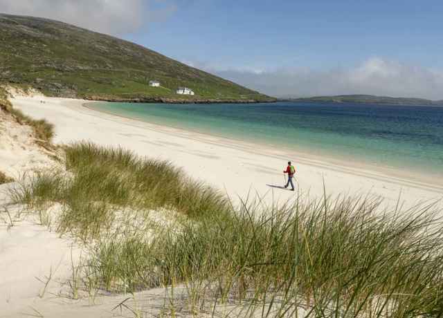 A hiker strolling along a deserted golden sandy beach on Barra.