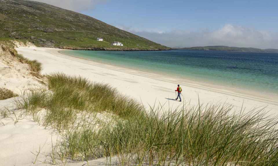 A hiker strolling along a deserted golden sandy beach on Barra.
