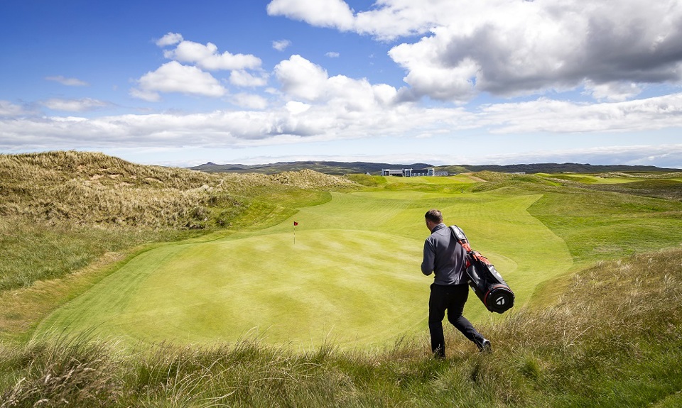 Man on golf course walking in the sun to green with his golf bag