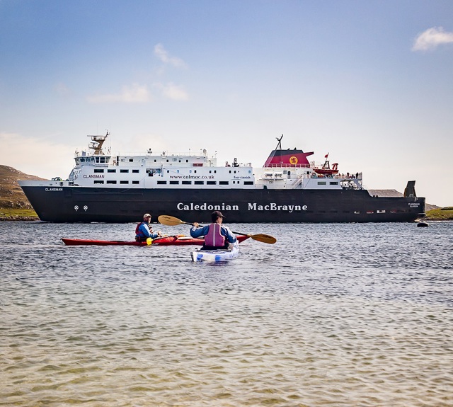Two people rowing in kayaks with the CalMac ferry MV Clansman in sailing past in the background.