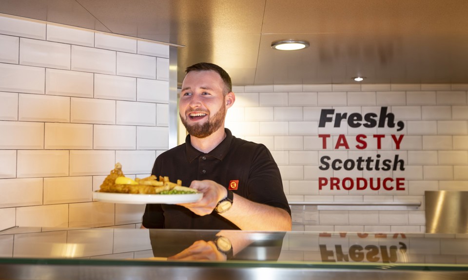 a server passing a plate of fish, fries and peas to a customer from the servery