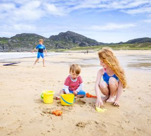 Children at the beach building sandcastles with yellow buckets and spades