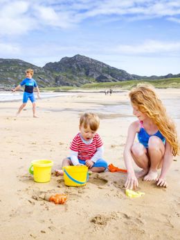 Children at the beach building sandcastles with yellow buckets and spades